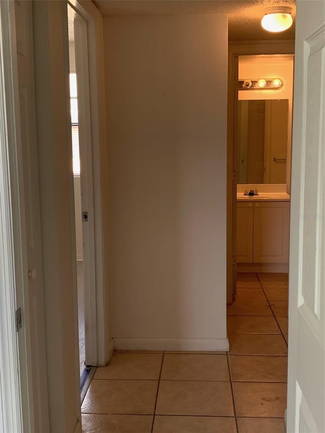 corridor featuring light tile patterned floors, baseboards, and a sink