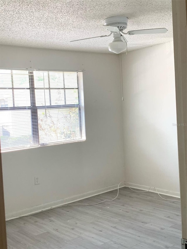 spare room with baseboards, a ceiling fan, light wood-style floors, and a textured ceiling