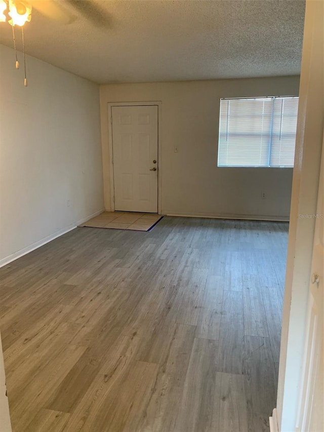 unfurnished room featuring a textured ceiling, wood finished floors, baseboards, and ceiling fan