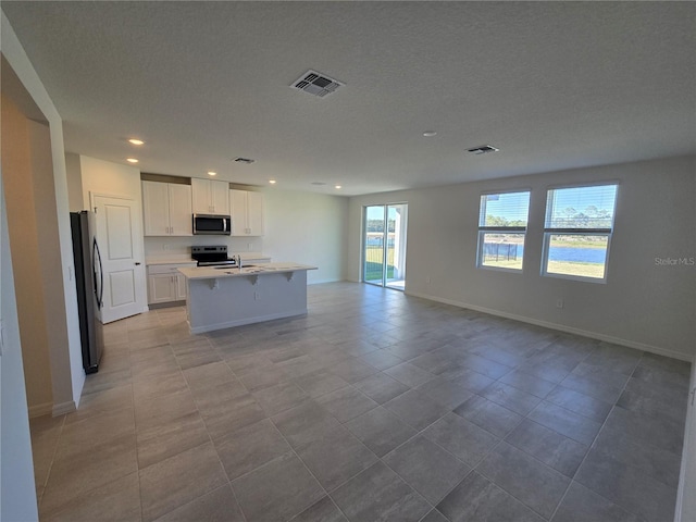 kitchen featuring stainless steel appliances, visible vents, open floor plan, light countertops, and a center island with sink