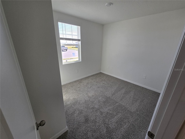 spare room featuring dark colored carpet and baseboards