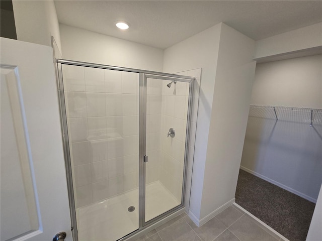 full bath featuring a shower stall, baseboards, a walk in closet, and tile patterned floors