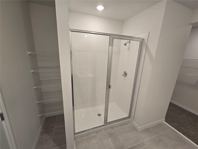 bathroom featuring a stall shower, tile patterned flooring, a spacious closet, and baseboards