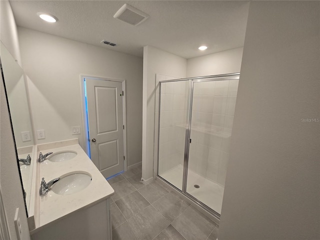 full bath featuring visible vents, a sink, a shower stall, and double vanity