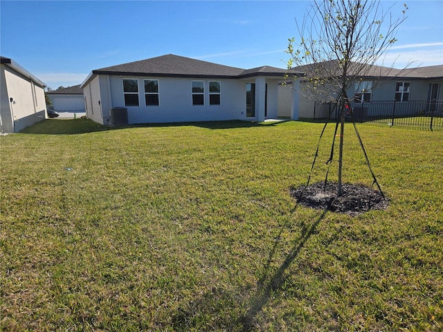 rear view of house featuring central AC, fence, a lawn, and stucco siding