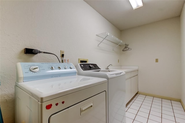 washroom with cabinet space, light tile patterned floors, baseboards, washing machine and clothes dryer, and a sink