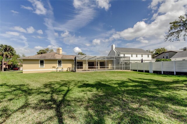 rear view of property with glass enclosure, a lawn, a chimney, and fence