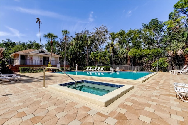 community pool with fence, a hot tub, and a patio