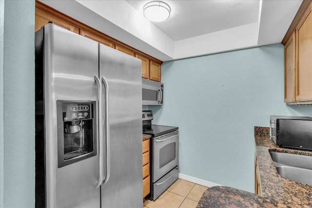 kitchen featuring light tile patterned floors, baseboards, appliances with stainless steel finishes, and brown cabinets