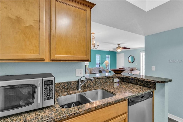 kitchen featuring ceiling fan, open floor plan, dark stone countertops, stainless steel appliances, and a sink