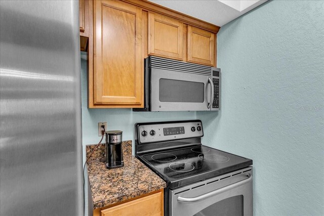 kitchen with appliances with stainless steel finishes, brown cabinets, and a textured wall