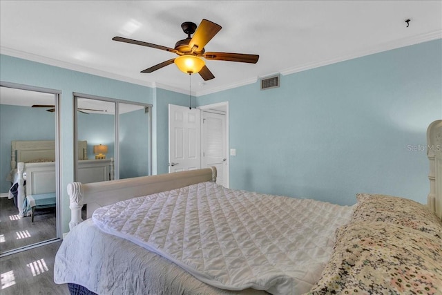 bedroom with visible vents, a ceiling fan, ornamental molding, wood finished floors, and two closets