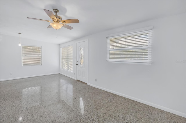 empty room with ceiling fan, speckled floor, plenty of natural light, and baseboards