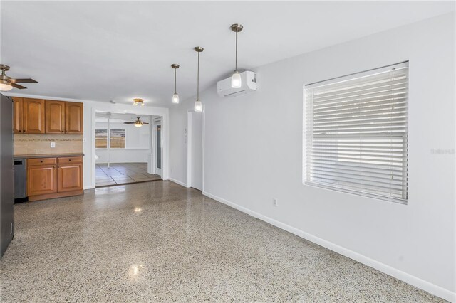 interior space with brown cabinets, a wall unit AC, stainless steel dishwasher, a ceiling fan, and speckled floor