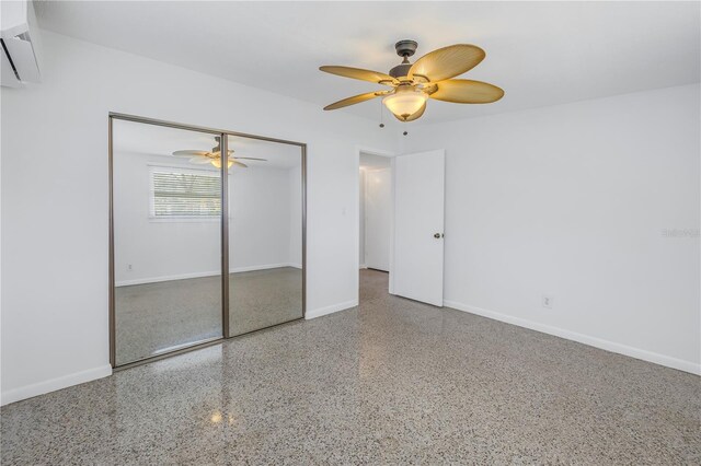 unfurnished bedroom featuring ceiling fan, a wall unit AC, speckled floor, baseboards, and a closet