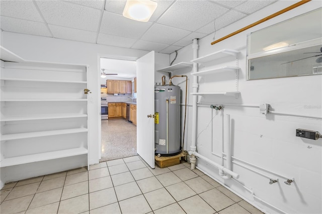 basement with a sink, light tile patterned floors, water heater, and a drop ceiling