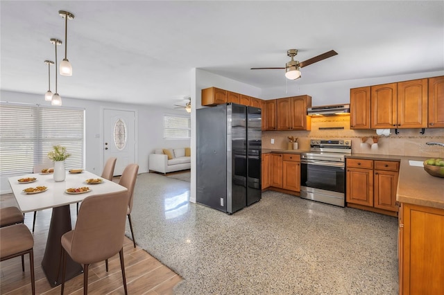 kitchen featuring under cabinet range hood, brown cabinetry, freestanding refrigerator, and stainless steel range with electric cooktop