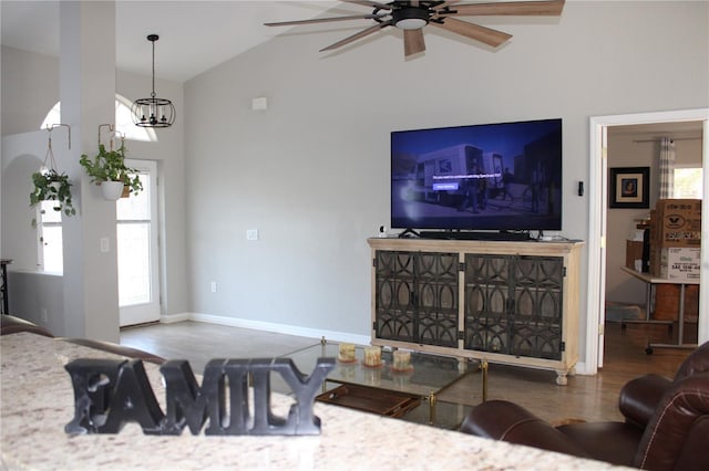 living room with ceiling fan with notable chandelier, high vaulted ceiling, wood finished floors, and baseboards