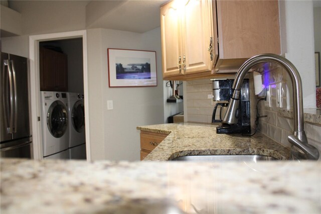 kitchen with tasteful backsplash, light stone counters, freestanding refrigerator, washer and dryer, and a sink