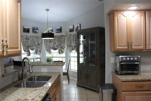 kitchen featuring a toaster, light tile patterned floors, tasteful backsplash, a sink, and light stone countertops