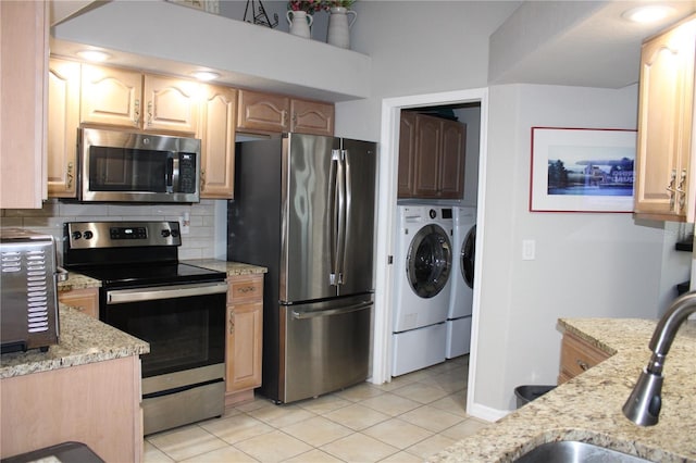 kitchen featuring light tile patterned floors, light stone counters, appliances with stainless steel finishes, decorative backsplash, and washer and clothes dryer