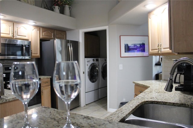 kitchen with decorative backsplash, appliances with stainless steel finishes, a sink, light stone countertops, and washer and dryer