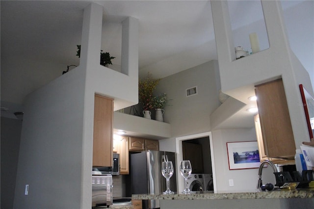 kitchen with visible vents, a towering ceiling, freestanding refrigerator, separate washer and dryer, and a sink