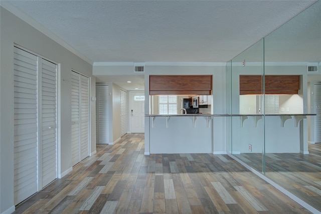 kitchen with a textured ceiling, a breakfast bar area, wood finished floors, and visible vents