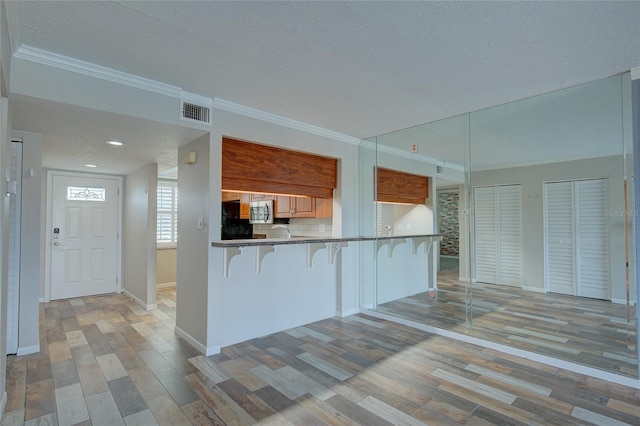 kitchen featuring ornamental molding, a breakfast bar, stainless steel microwave, and visible vents