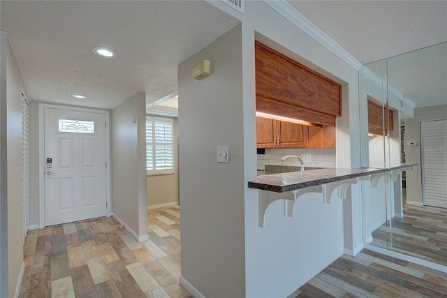 kitchen featuring tasteful backsplash, a breakfast bar area, a textured ceiling, crown molding, and light wood-type flooring