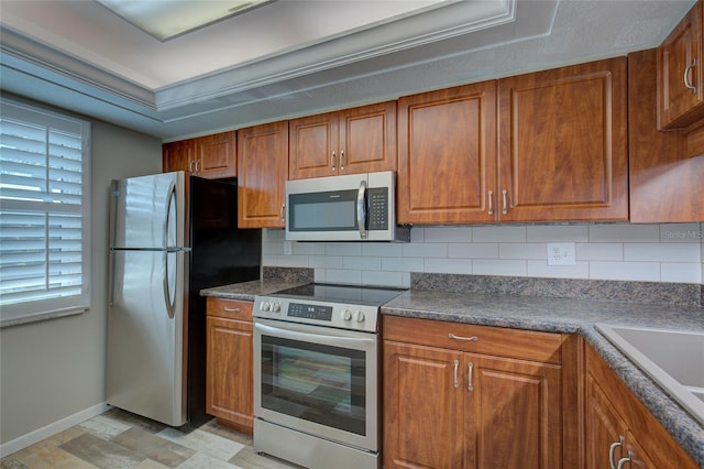 kitchen featuring appliances with stainless steel finishes, dark countertops, decorative backsplash, and brown cabinets