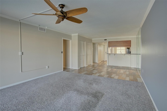 unfurnished living room with crown molding, visible vents, light carpet, a textured ceiling, and baseboards