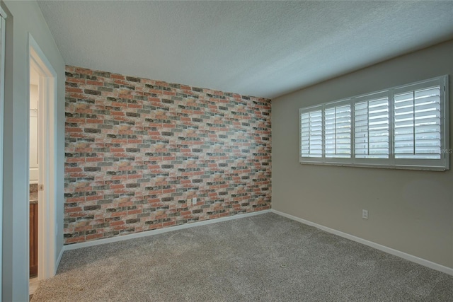 spare room with a textured ceiling, brick wall, carpet, and baseboards