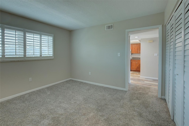 empty room with baseboards, a textured ceiling, visible vents, and light colored carpet