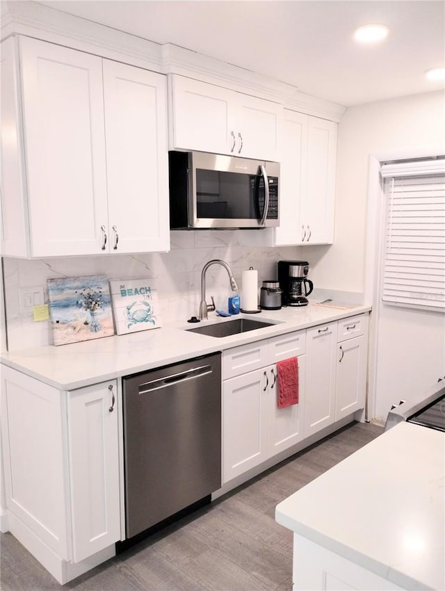 kitchen featuring light countertops, decorative backsplash, appliances with stainless steel finishes, white cabinetry, and a sink