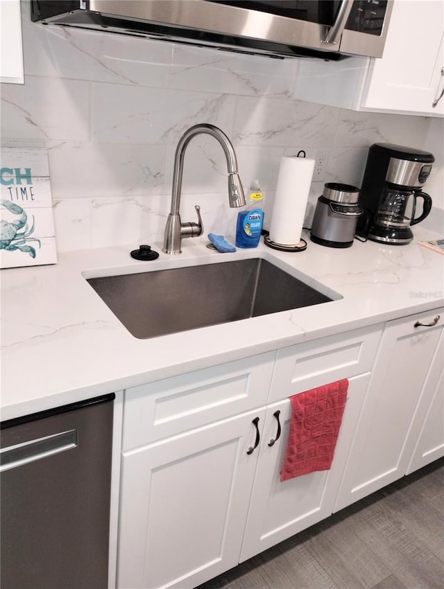 kitchen with light stone counters, a sink, white cabinets, stainless steel dishwasher, and decorative backsplash