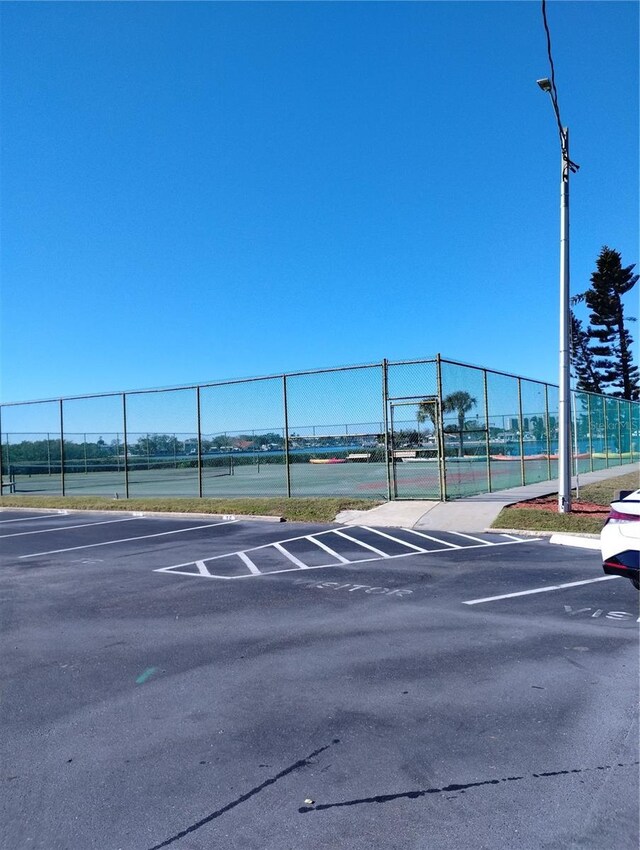 uncovered parking lot featuring a tennis court and fence