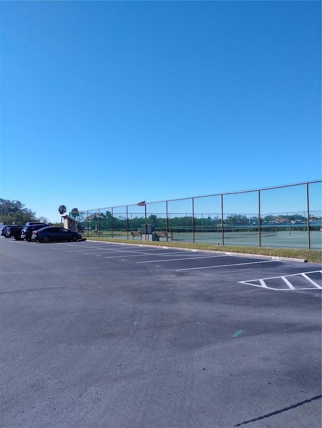 uncovered parking lot with a tennis court and fence