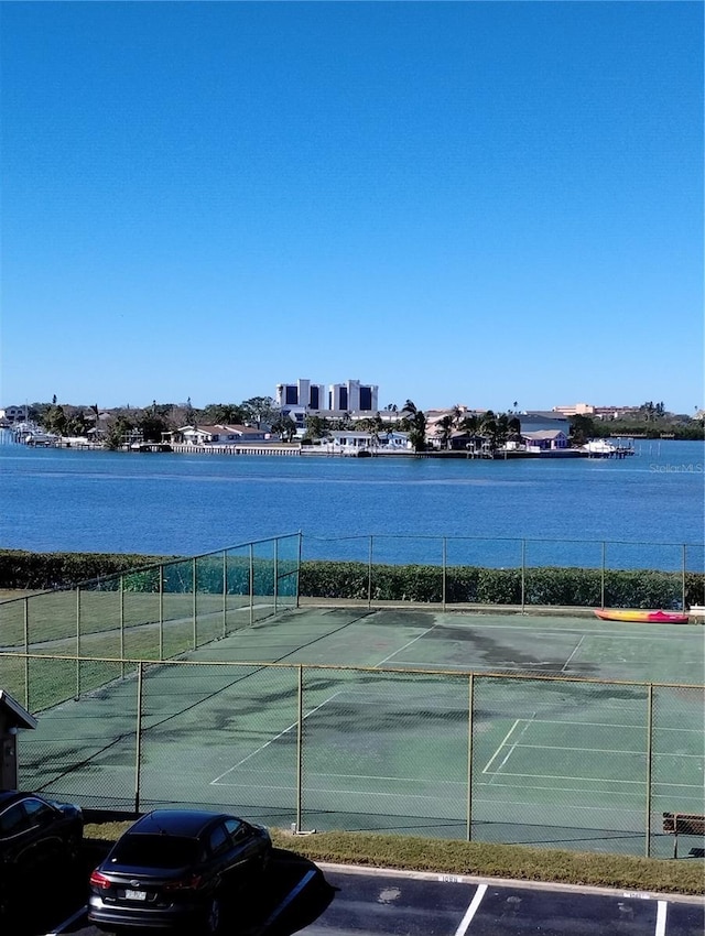 view of tennis court with a water view and fence