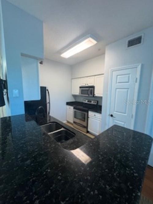 kitchen with visible vents, white cabinets, appliances with stainless steel finishes, a peninsula, and a sink