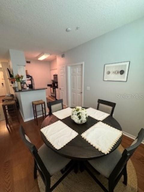 dining space featuring a textured ceiling, baseboards, and wood finished floors