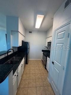 kitchen with light tile patterned floors, visible vents, white cabinets, dark countertops, and a sink