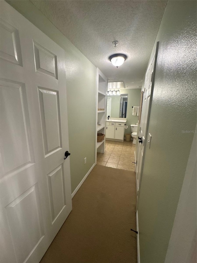 hall featuring a textured ceiling, light tile patterned floors, and baseboards