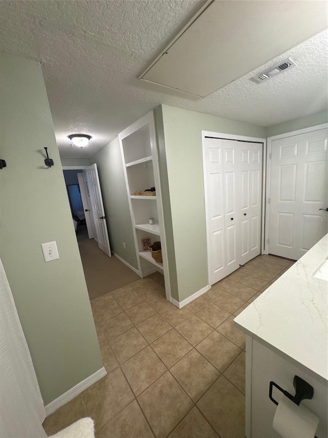 corridor with baseboards, visible vents, a textured ceiling, and light tile patterned flooring