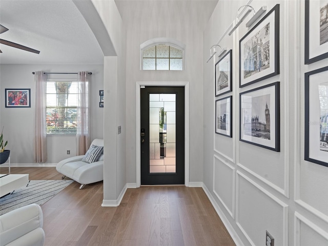 entryway with arched walkways, wood finished floors, a ceiling fan, and baseboards