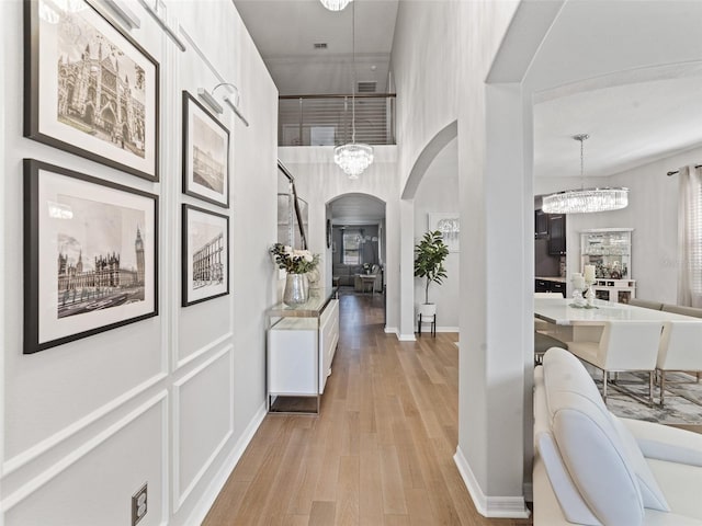 corridor featuring arched walkways, a notable chandelier, visible vents, baseboards, and light wood-type flooring