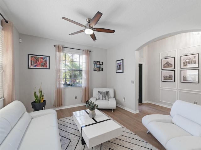 living room featuring a ceiling fan, arched walkways, baseboards, and wood finished floors