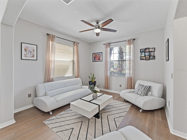 living room with a ceiling fan, light wood-type flooring, a textured ceiling, and baseboards