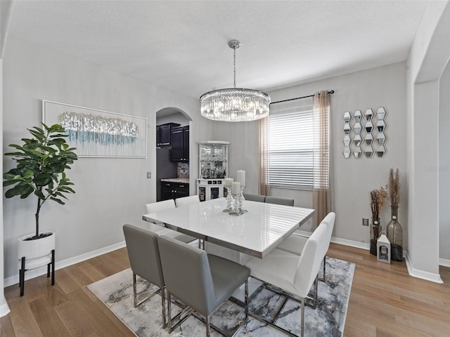 dining room with light wood-style floors, arched walkways, a textured ceiling, and baseboards