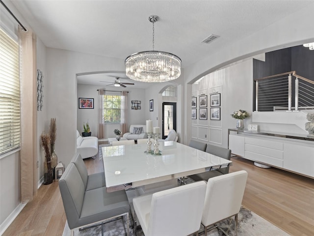 dining area with light wood-style flooring, visible vents, arched walkways, and baseboards